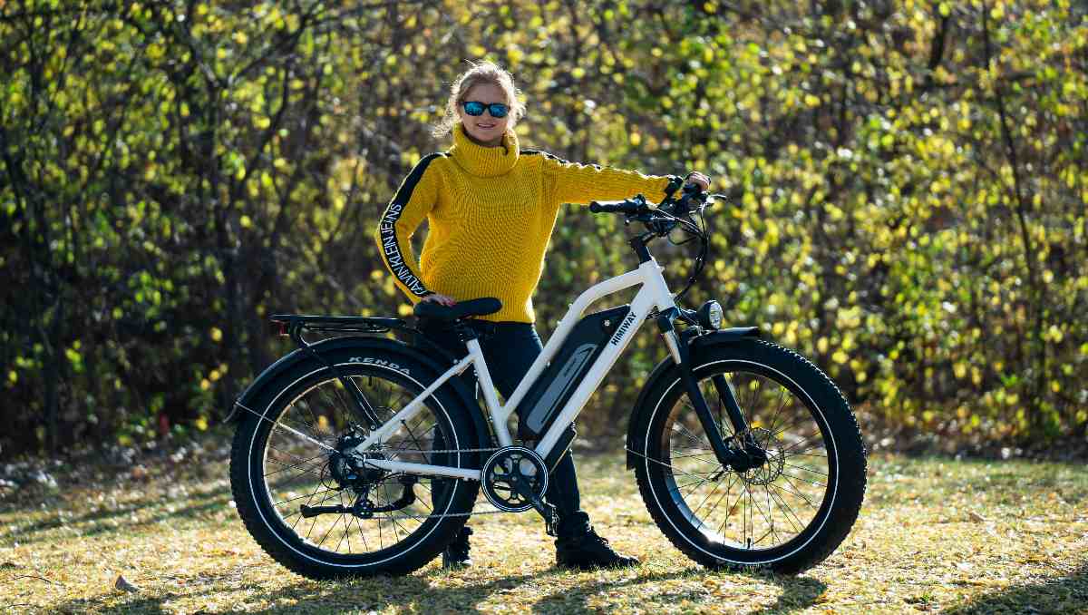 Girl wearing yellow shirt standing beside an e-bike under the sun